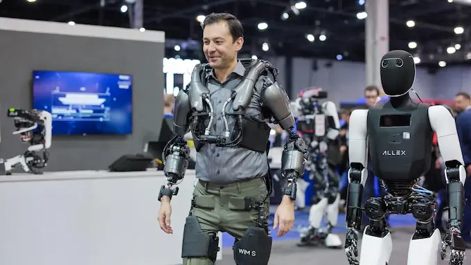  Person testing the WIM S wearable walking-assist robot at a CES-style expo for a Weekly Robotics News feature