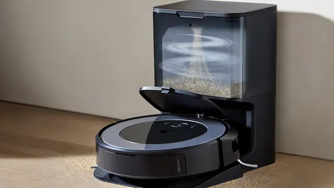 “Roomba robot vacuum docking at a self-emptying station that sucks debris into a bag”